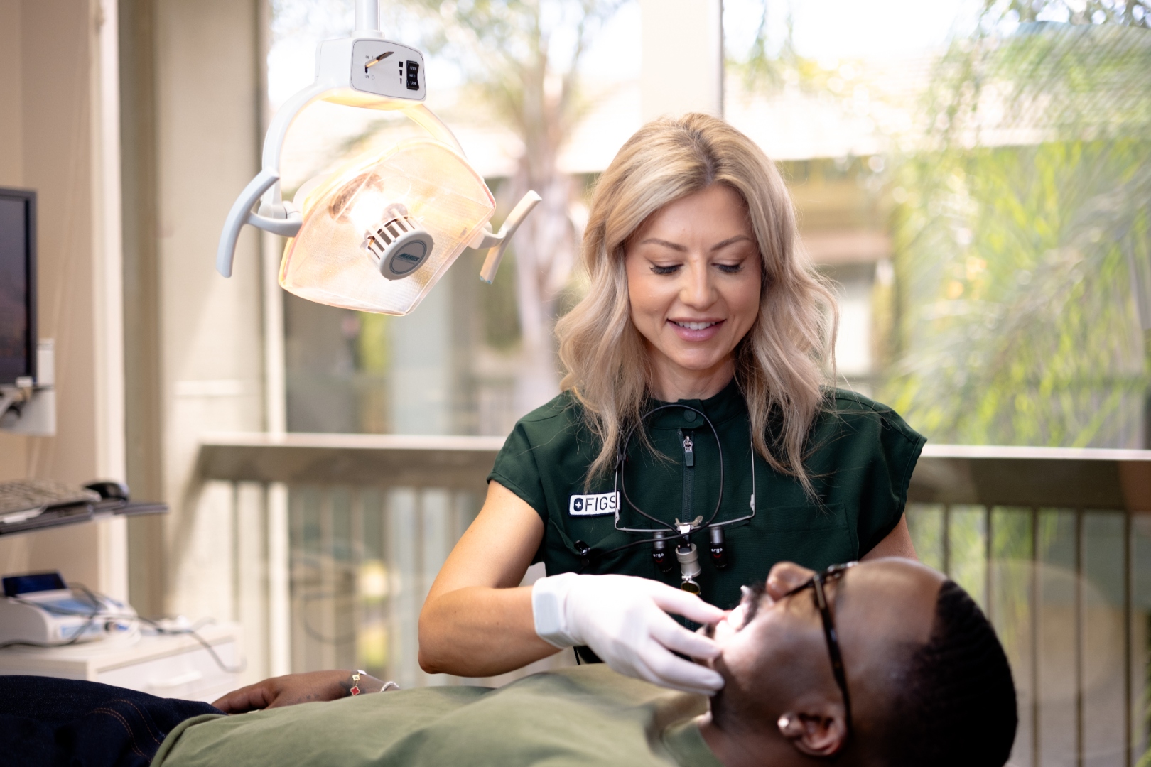 Brenda Powers working with a patient, forest green scrubs, bright window with palm trees